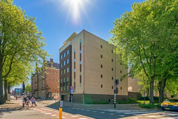 Modern appartementencomplex aan de Prins Hendrikkade in het zonlicht, omgeven door bomen en stadsverkeer.